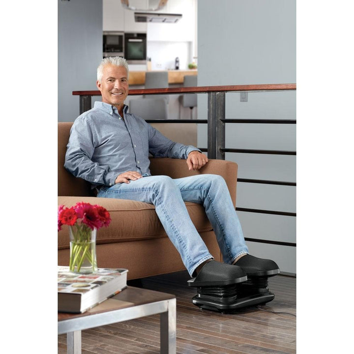 Man sits in chair with both feet in the Homedics Shiatsu Flex Foot & Ankle Massager with Heat