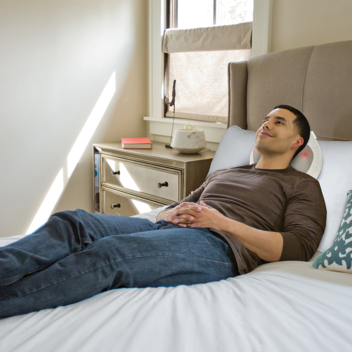 Man relaxes on bed while receiving a massage from the Homedics Total Recline Neck Massager