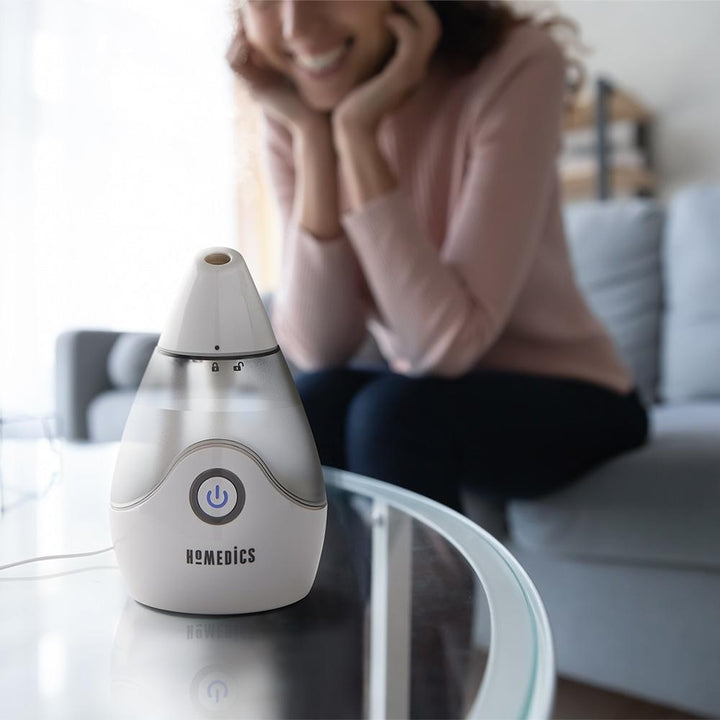 Woman smiles while looking at Homedics TotalComfort Personal Ultrasonic Humidifier on table