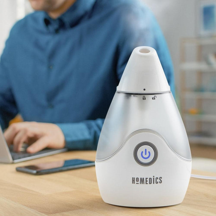 Man types on laptop at computer desk with the Homedics TotalComfort Personal Ultrasonic Humidifier next to him