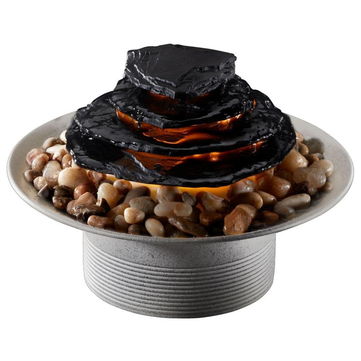 Woman sits in chair next to Homedics Mirra Zen Tabletop Relaxation Fountain on table