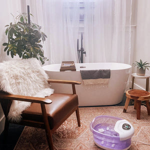 Bathroom view with chair next to a bathtub with the Salt-N-Soak Footbath with Heat Boost on the floor
