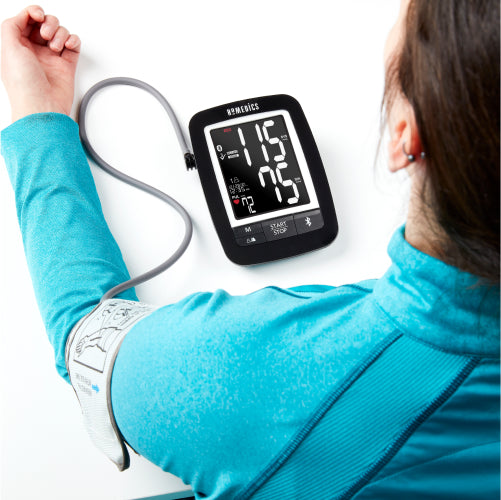 Woman in blue shirt sits at table as blood pressure is taken with the Homedics Premium Arm Blood Pressure Monitor
