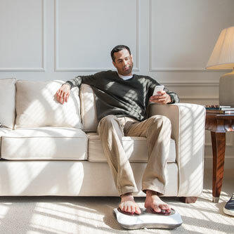 Man sits on couch with feet on the Homedics Shiatsu Deluxe Foot Massager with Heat