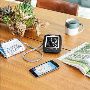 Homedics Premium Arm Blood Pressure Monitor sits on table next to phone, cup of coffee, and magazine