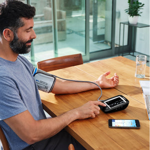 Man sits at table as blood pressure is taken with the Homedics Premium Arm Blood Pressure Monitor