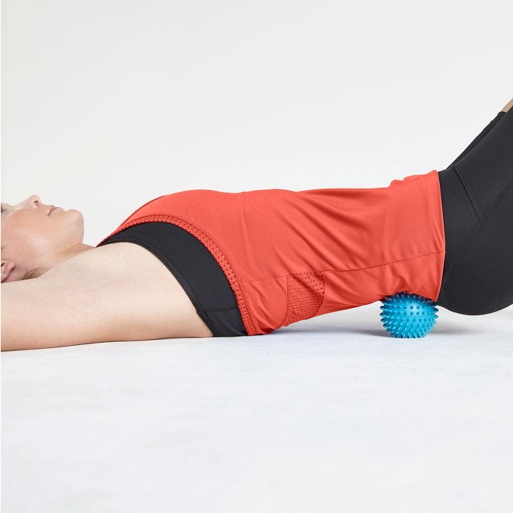 Woman stretched out on floor massages lower back with the Homedics Atlas Vibration Acu-Node Massager