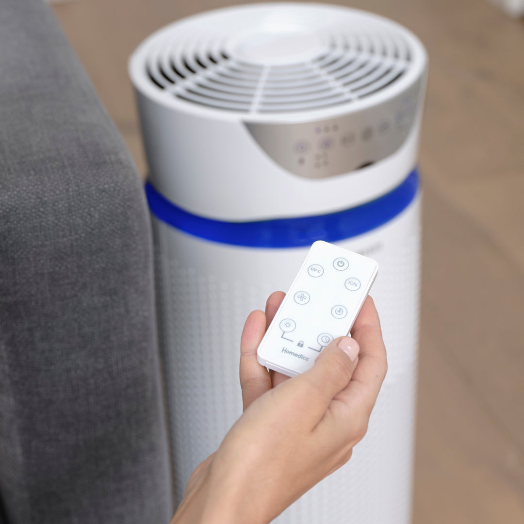 White | hand holding the remote that allows you to adjust settings on the Homedics TotalClean 5-in-1 UV-C Deluxe Large Room Air Purifier