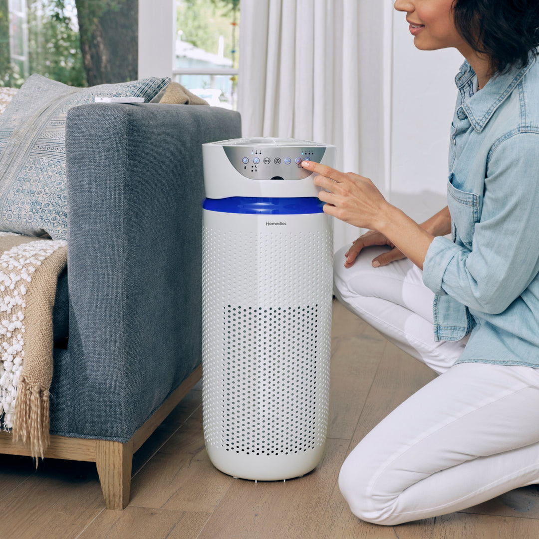 White | Woman kneels to adjust settings on the Homedics TotalClean 5-in-1 UV-C Deluxe Large Room Air Purifier in her living room
