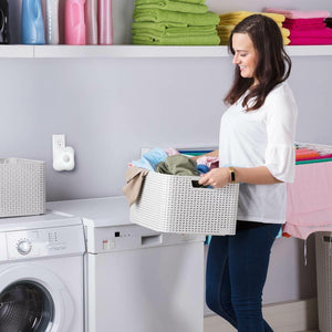 Woman holds laundry basket with the Homedics TotalClean Personal UV Air Sanitizer attached to wall outlet above washer