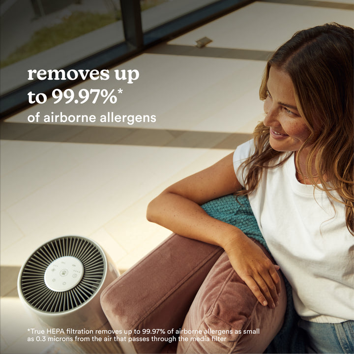 Woman sitting with the Homedics TotalClean PetPlus 5-in-1 Air Purifier that removes 99.97% airborne allergens.