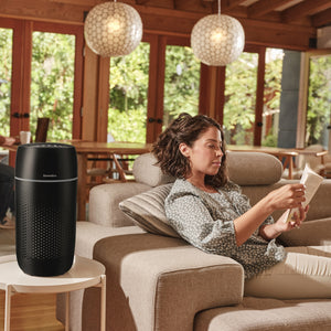 Black | Medium Room Tower Air Purifier T22 purifies the air in the room while the woman reclines on a couch reading a book