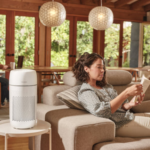 White | Medium Room Tower Air Purifier T22 purifies the air in the room while the woman reclines on a couch reading a book