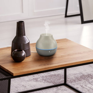 Homedics® Diffuser is kept on wooden centre table beside two beautiful vase and steam is coming out of it