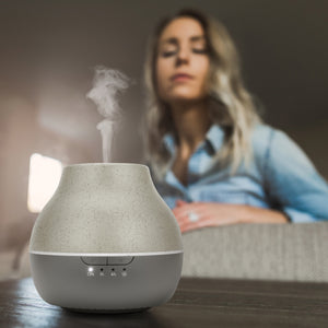 Steam is coming out of Homedics® diffuser and a woman inhales the same for calm experience.