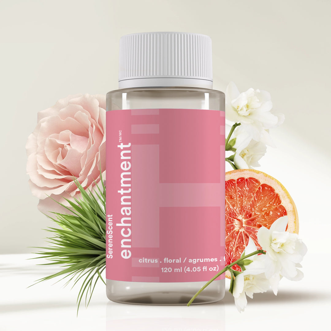 Bottle of SereneScent™ Enchantment with flowers and a grapefruit slice on a light background.