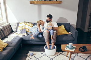 Family sitting on the couch while Dad relaxes by putting his feet into the Shiatsu Bliss Foot Spa with Heat Boost