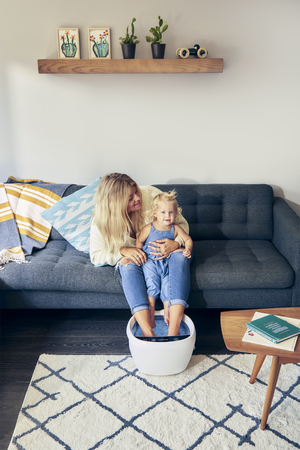 Woman playing with child as she also relaxes by putting her feet into the Shiatsu Bliss Foot Spa with Heat Boost