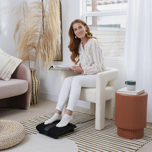 Woman sits in chair and reads while enjoying a foot massage from the Homedics Triple Action Shiatsu Foot Massager with Heat