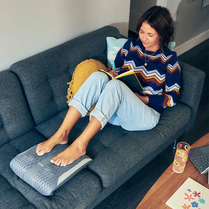 Woman lays across couch while massaging her feet with the Homedics Gentle Touch Gel Shiatsu Foot Massager with Soothing Heat