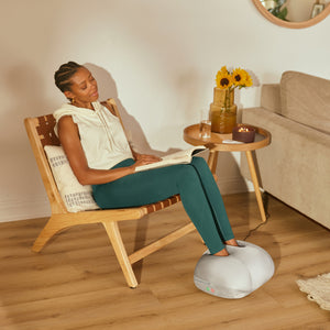 Homedics® 3-in-1 Shiatsu Massager massages her feet while she relaxes on a chair reading a book