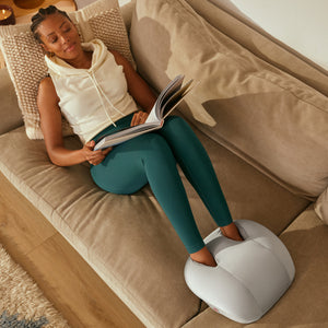 Homedics® 3-in-1 Shiatsu Massager continues to enjoy a foot massage on the couch as she reads a magazine