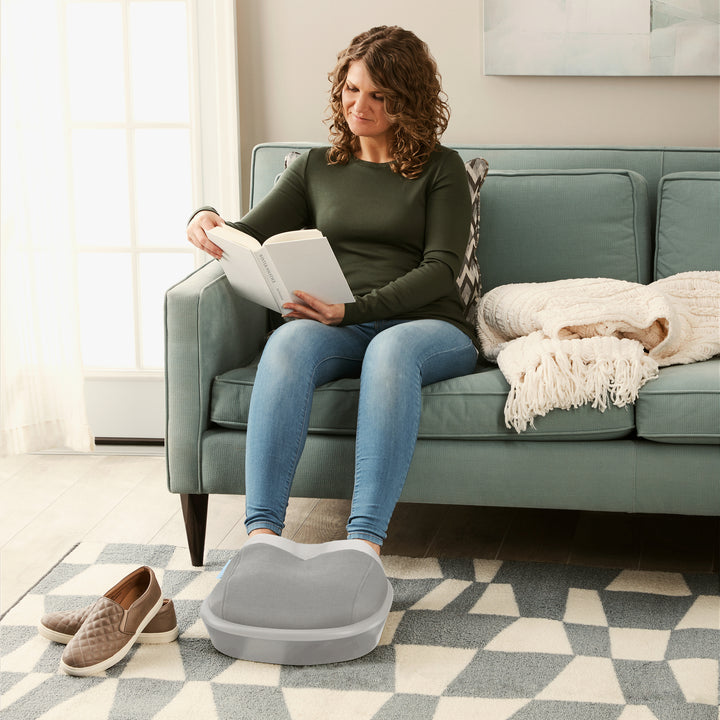 Woman sitting on the couch using the Homedics® Shiatsu Air Max Foot Massager while reading