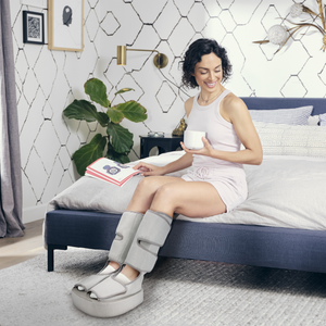 Woman sitting on ben relaxing with coffee wearing her Homedics Real Relief Leg & Foot Massager