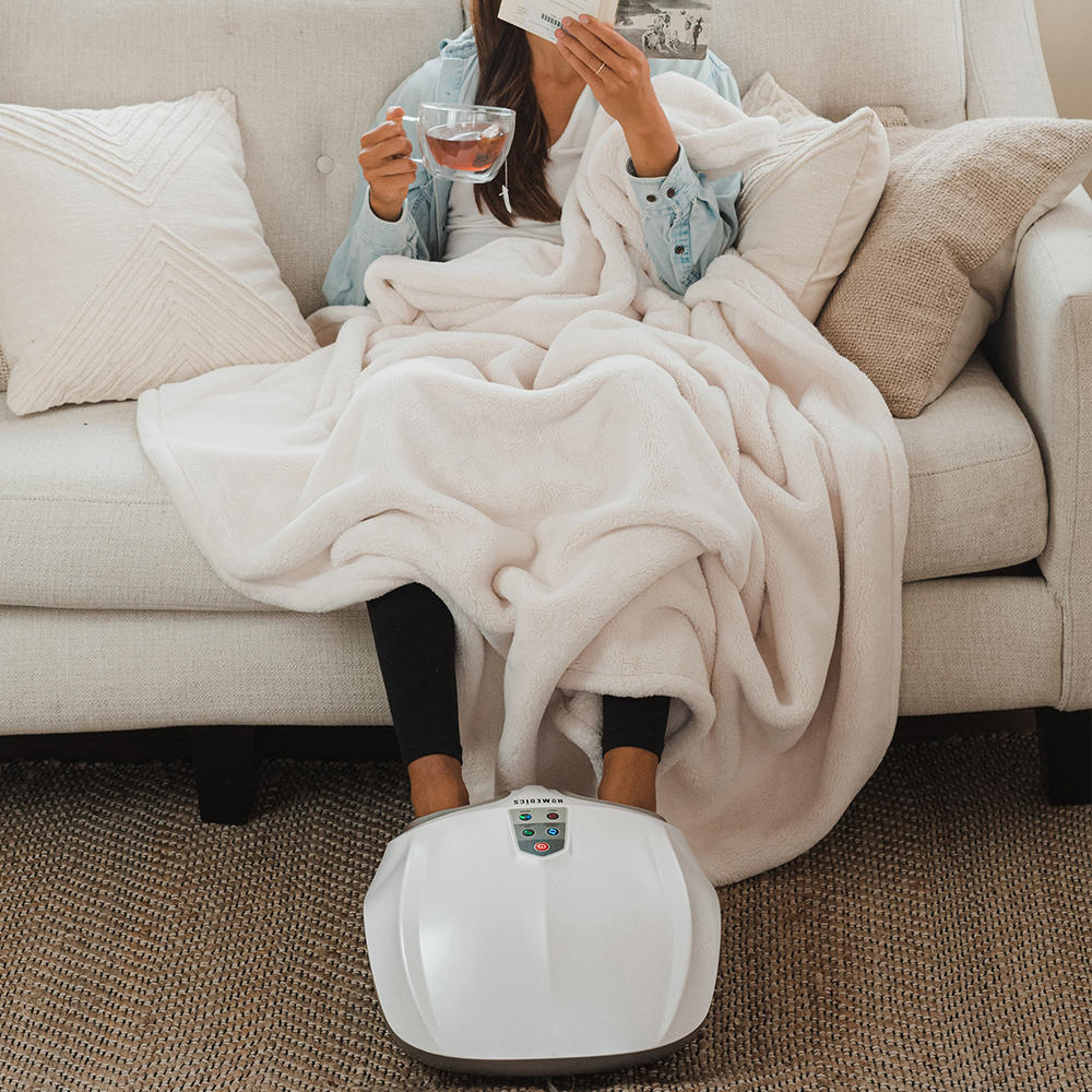Woman sits on couch wrapped in blanket while enjoying a massage from the Homedics Shiatsu Air 2.0 Foot Massager with Heat