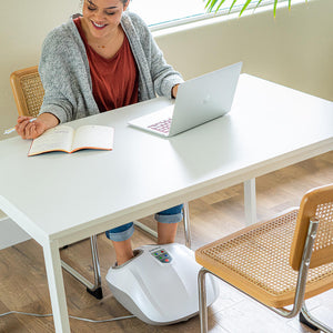 Woman sits at table working on laptop while enjoying a massage from the Homedics Shiatsu Air 2.0 Foot Massager with Heat