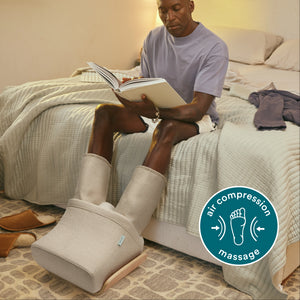 Full view of man sitting on bed using Homedics® Compression Boot Foot & Calf Massager with Heat while reading