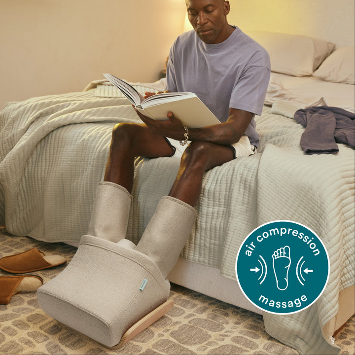 Full view of man sitting on bed using Homedics® Compression Boot Foot & Calf Massager with Heat while reading