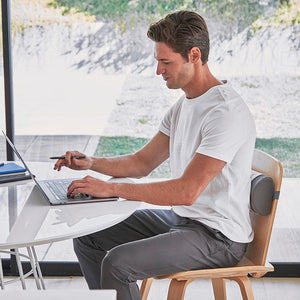 Man sitting at desk typing on laptop enjoys back relief using Homedics Lumbar Pillow with Soothing Heat attached to chair