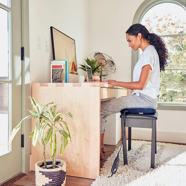 Alternate view of woman sitting on the Homedics Contoured Seat Cushion with Heat while seated in a chair at desk typing on laptop