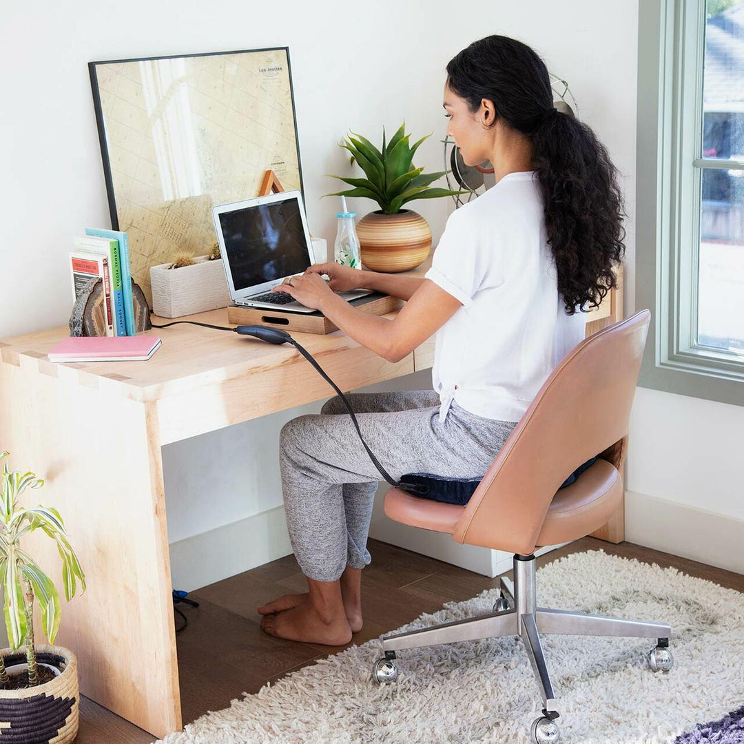 Woman sits on the Homedics Contoured Seat Cushion with Heat while seated in a chair at desk typing on laptop
