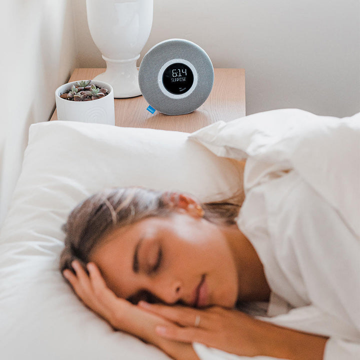 Woman sleeping in bed with the Homedics Deep Sleep Revitalize Engineered Sleep Sound Alarm Clock in background on night stand