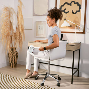 A woman sits in a chair and uses the Homedics® Duo Percussion Body Massager with Heat on her outer thigh