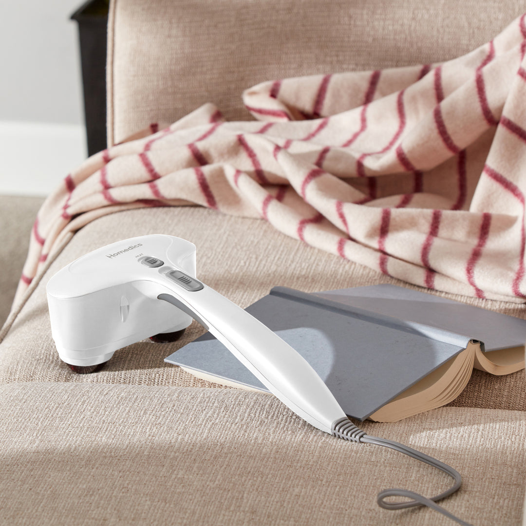 Homedics® Duo Percussion Body Massager with Heat lays on the couch next to an open book