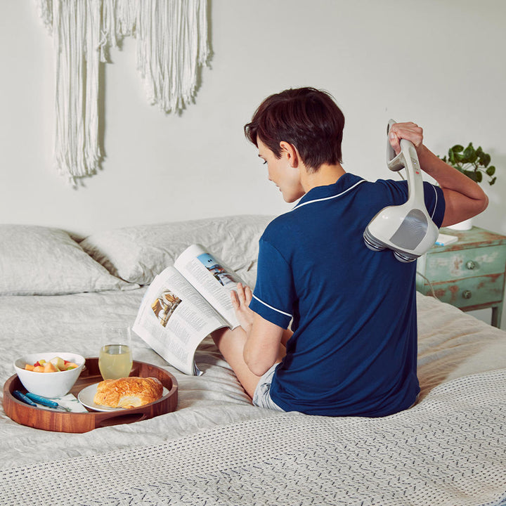 Brown | Woman sits on bed reading book while enjoying shoulder massage with the Homedics Percussion Action Plus Handheld Massager with Heat