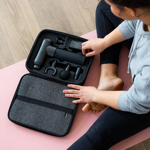 Woman sitting on floor opens carrying case for the Homedics Therapist Select Pro Percussion Massager