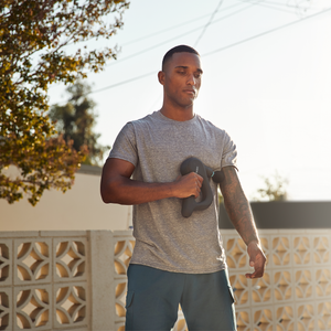 Man standing outdoors massaging his arm with the Homedics Therapist Select DuoTemp Pro Percussion Massager