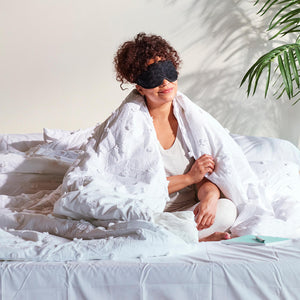 Woman sits up in bed covered with blanket while wearing the Homedics Gel Eye Mask with Hot and Cold Therapy