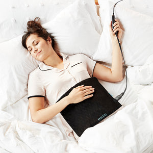 Woman relaxes in bed with the Homedics Weighted Hot & Cold Gel Heating Pad on abdomen