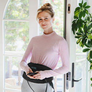 Woman smiles while turning on her Homedics Women’s Health Abdomen and Lower Back Hot & Cold Gel Therapy Belt