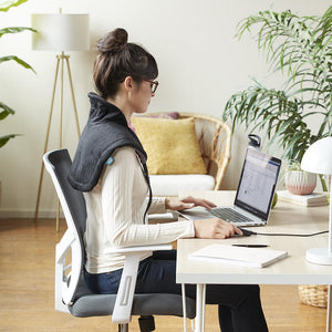 Alternate view of woman wearing the Homedics Weighted Gel Wrap on her shoulders while working at home office desk in brightly lit room