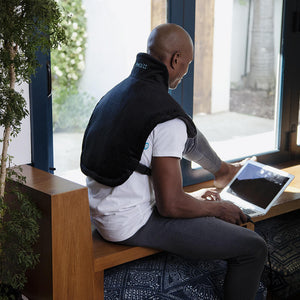 Man sits and works on laptop while wearing the Homedics Weighted Gel Back Wrap