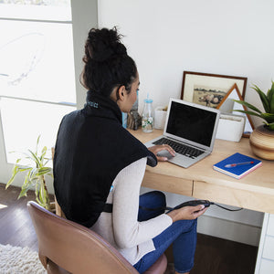 Woman works on laptop at office desk while wearing the Homedics Weighted Gel Back Wrap
