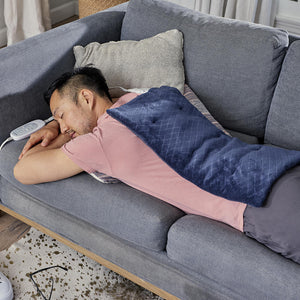 Man stretches out on couch while enjoying massage from the Homedics 12 x 24 Weighted Massaging Heating Pad