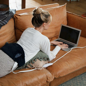 Woman lays across couch on her stomach working on laptop while wearing the Homedics Women's Health Comfort Heating Belt