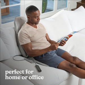 Man sits on the Homedics Shiatsu + Kneading and Vibration Massage Cushion with Heat on white couch while adjusting settings with controller